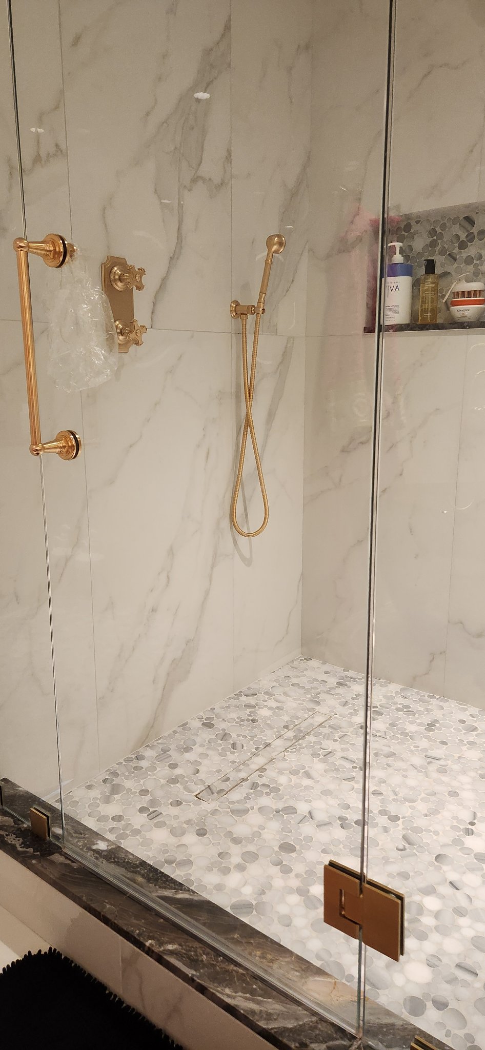Marble shower with gold handheld sprayer and tile niche