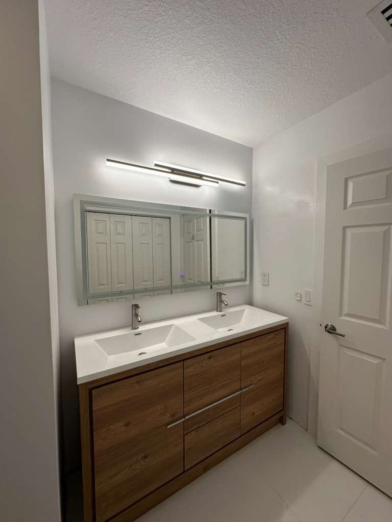Bathroom double vanity with wood cabinetry and modern light bar