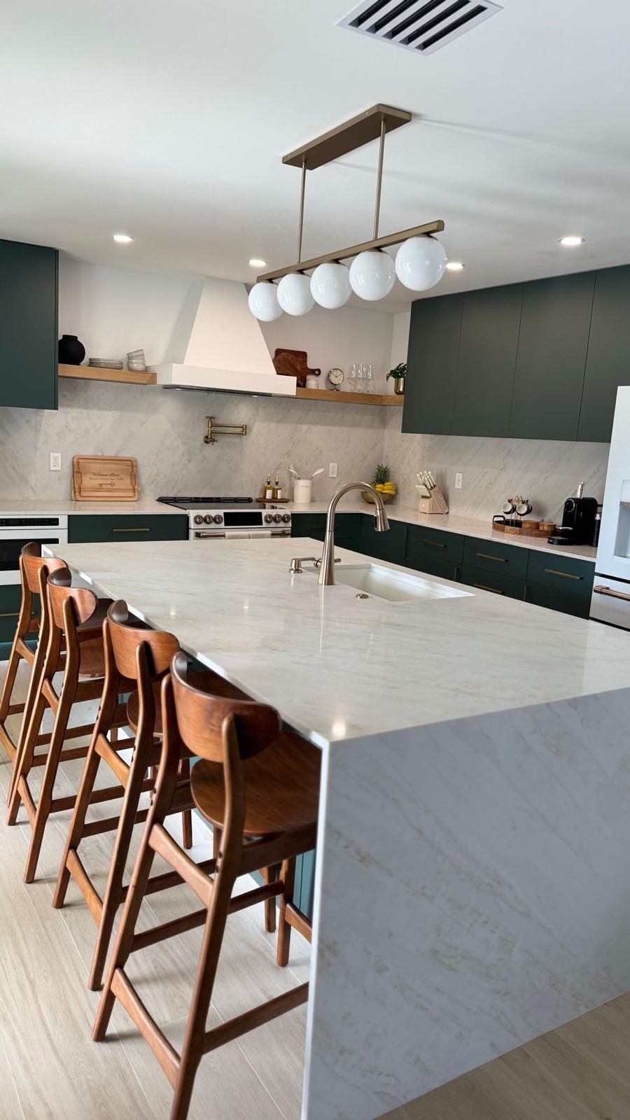 Dark green kitchen island with waterfall marble countertop and brass fixtures