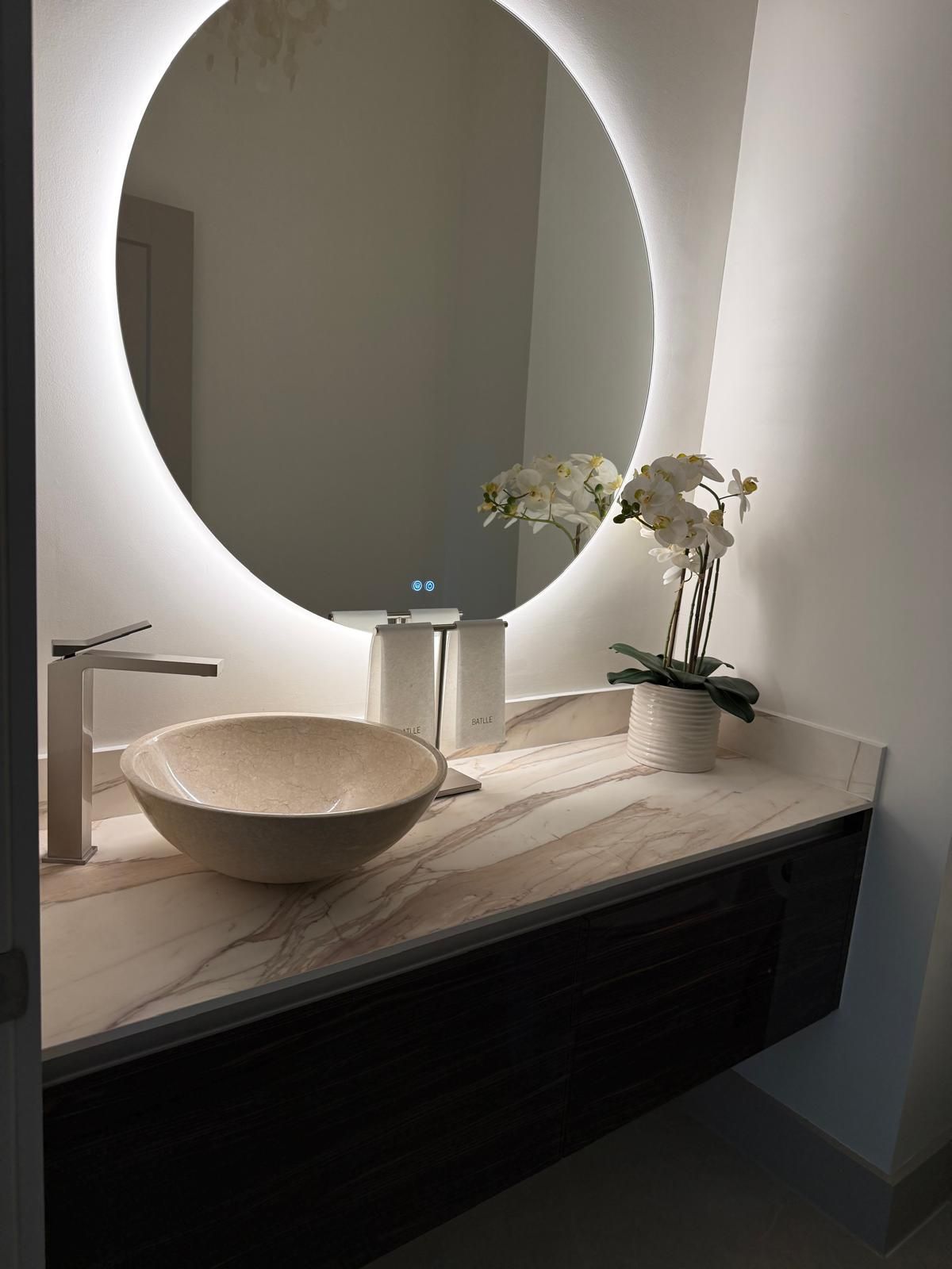 Luxury powder room with backlit round mirror and stone vessel sink