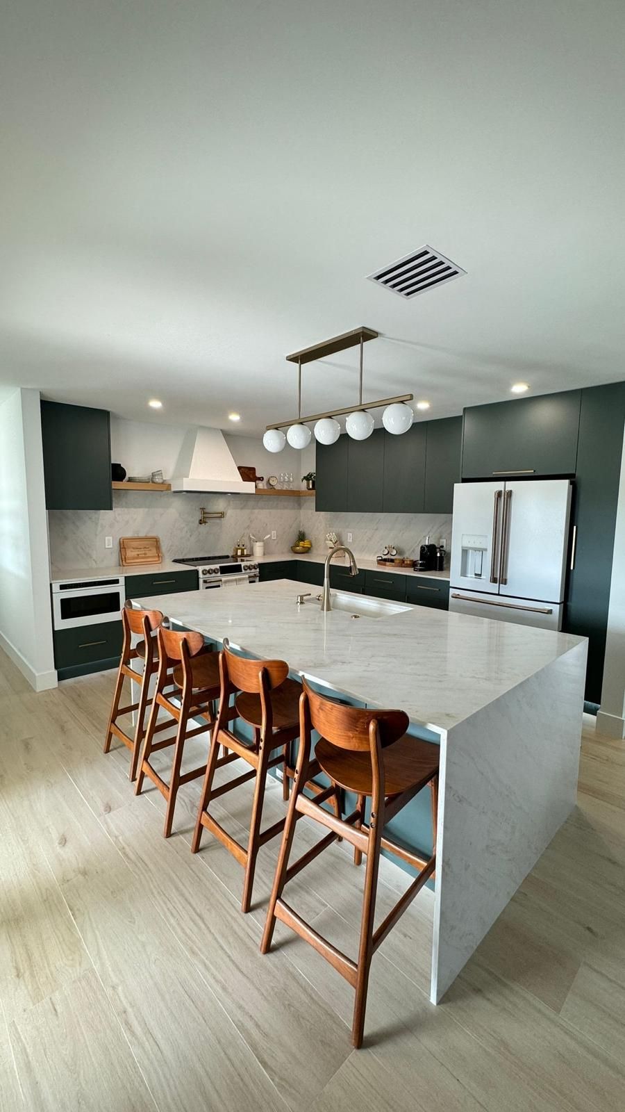 Designer kitchen with dark green cabinets and marble waterfall island
